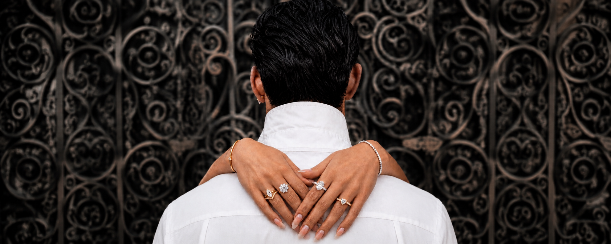 Woman wearing rings and bracelets embraces a man in front of ornate ironwork