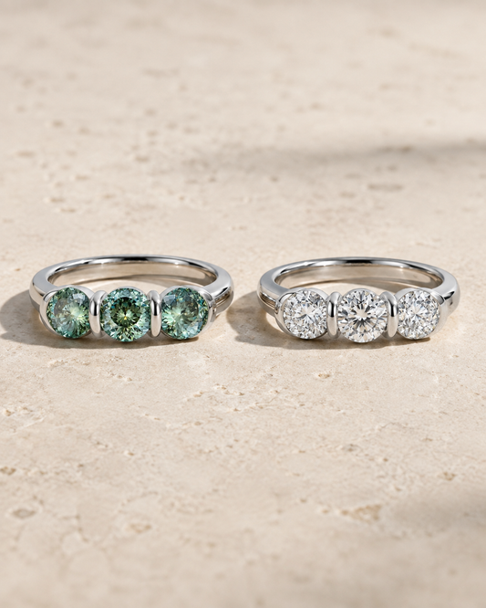 Three-stone moissanite rings with blue-green and white round stones displayed side by side