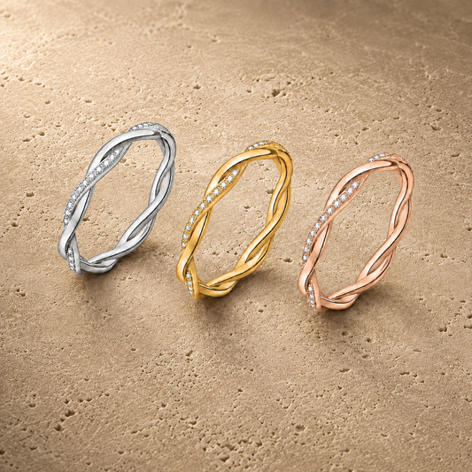 Twisted moissanite eternity rings in silver, gold and rose-gold tones on beige stone