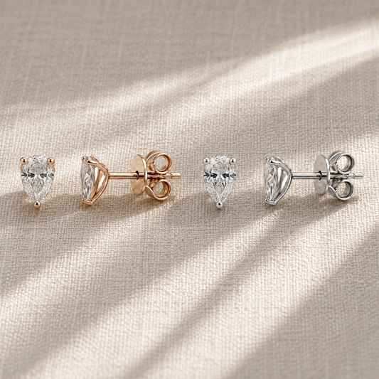Pear-cut moissanite stud earrings in white and rose gold-plated finishes on champagne fabric