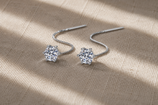 White gold-plated round moissanite threader earrings resting in soft curves on champagne fabric