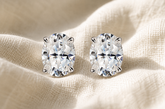 Pair of white gold-plated oval-cut moissanite stud earrings on champagne fabric