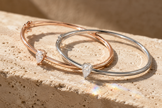 Pear-cut moissanite solitaire bangles in rose, yellow, and silver-tone finishes on beige stone
