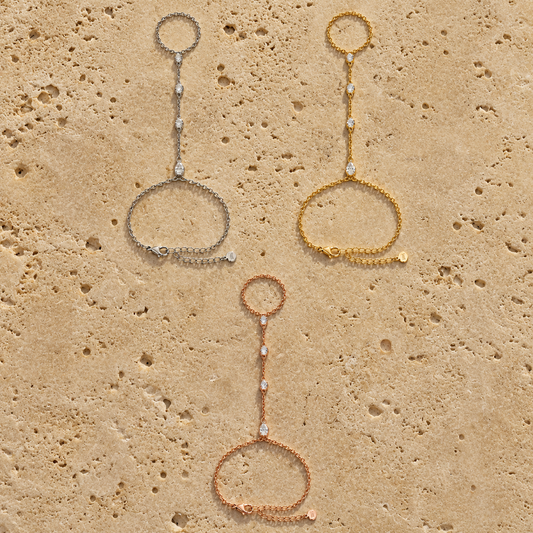 Pear-cut moissanite hand chain bracelets in silver, yellow, and rose-gold tones laid flat
