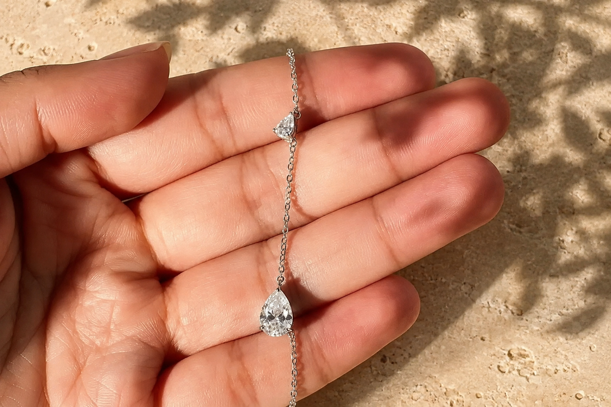 
שרשרת כסף 925 משובצת מואסנייט עם שתי אבנים בחיתוך אגס בציפוי זהב לבן 18 קראט מוחזקת בין האצבעות
