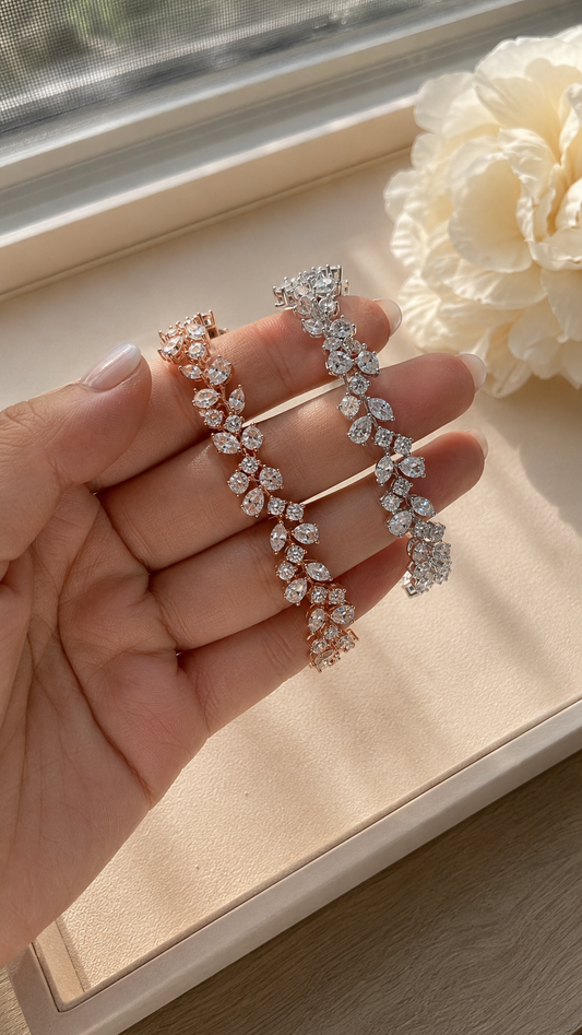 Rose- and silver-tone pear and round moissanite tennis bracelets held in a hand beside a sunlit window