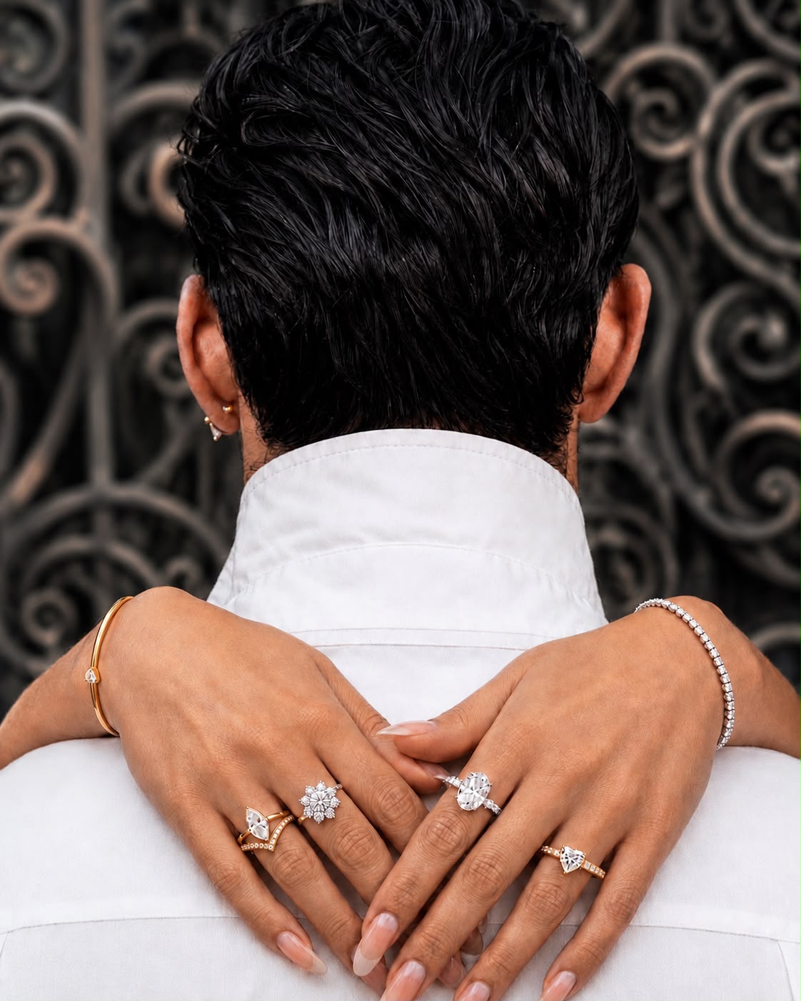 Woman wearing rings and bracelets embraces a man in front of ornate ironwork